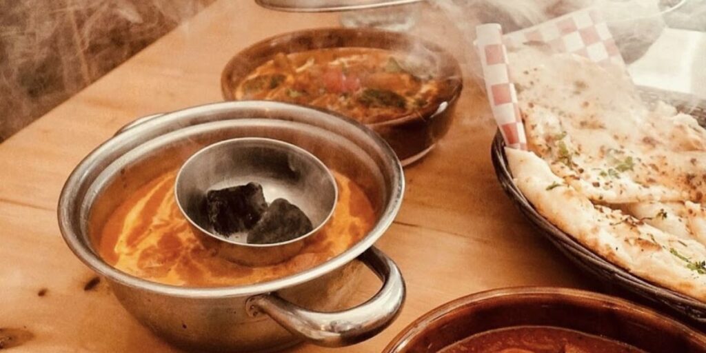 A table with several dishes of food, including butter chicken - succulent chicken in creamy tomato-based sauce with butter, cream, and spices.