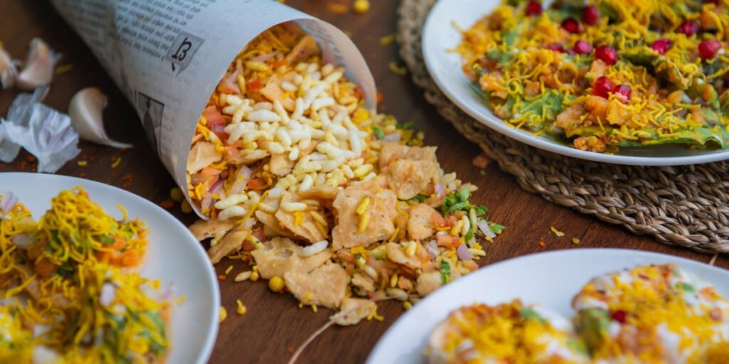 A table set with plates of Chaat Papri and Bhel Puri, alongside a newspaper.