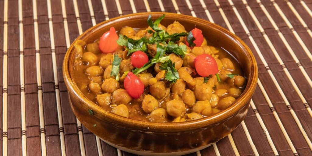 Indian chickpea curry (chole) in brown bowl on wooden table. Traditional Punjabi dish with fluffy fried bread (bhature).