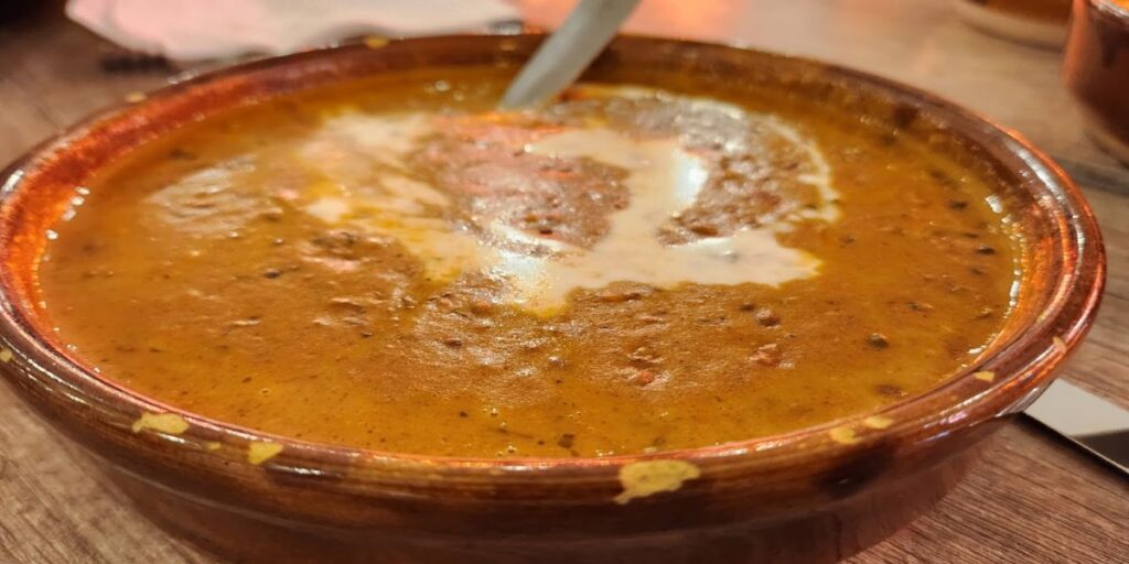 A bowl of creamy Dal Makhani soup with a spoon, made from black lentils and kidney beans, slow-cooked with butter and cream.