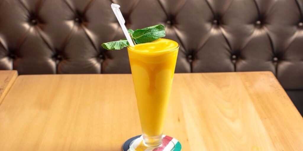 A glass of sweet mango lassi with a straw on a wooden table.