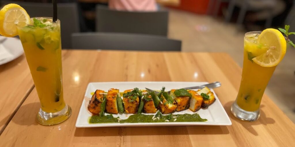 A plate with paneer tikka, a vegetarian treat of marinated Indian cottage cheese cubes grilled to perfection, served with drinks on a table.