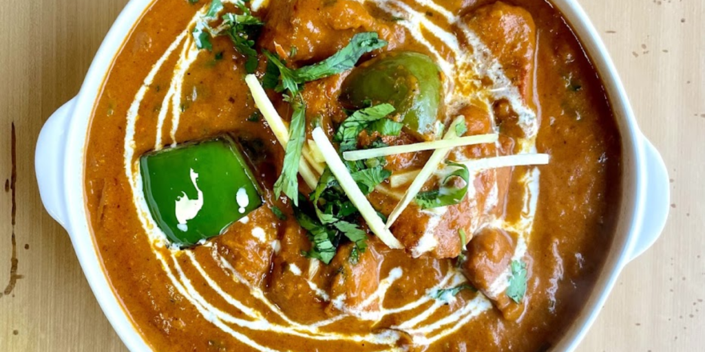 White bowl filled with curry, garnished with herbs - The Allure and Best Butter Chicken in Toronto