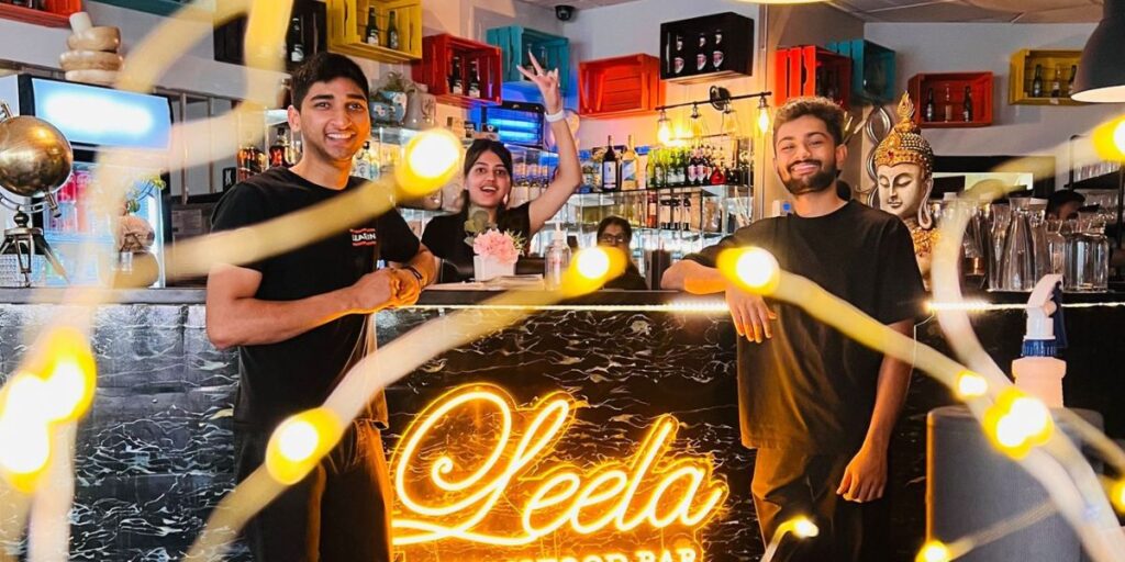 Three men standing behind a bar with lights, smiling and serving drinks.