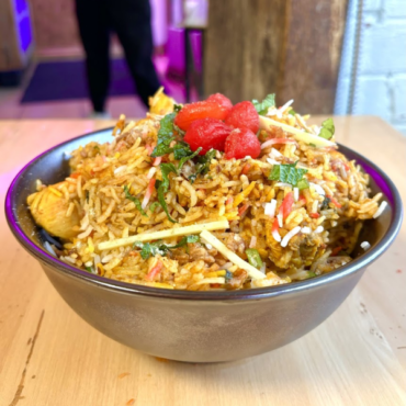 A bowl of biryani filled with rice and vegetables placed on a rustic wooden table, showcasing vibrant colors and textures.