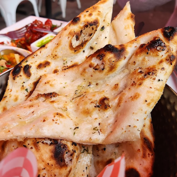 A plate of naan bread accompanied by a basket filled with assorted Indian breads, showcasing their diverse textures and colors.