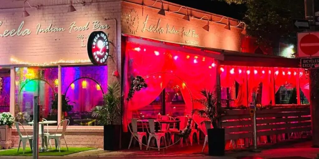 Exterior of Leela Indian Food Bar, featuring vibrant red lights, inviting guests to experience modern Indian cuisine.