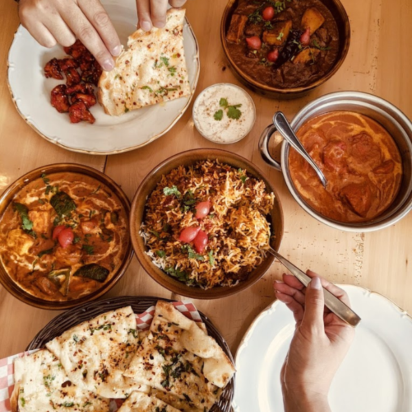 A table adorned with various Indian dishes, hands reaching for flavorful main courses, showcasing culinary diversity.