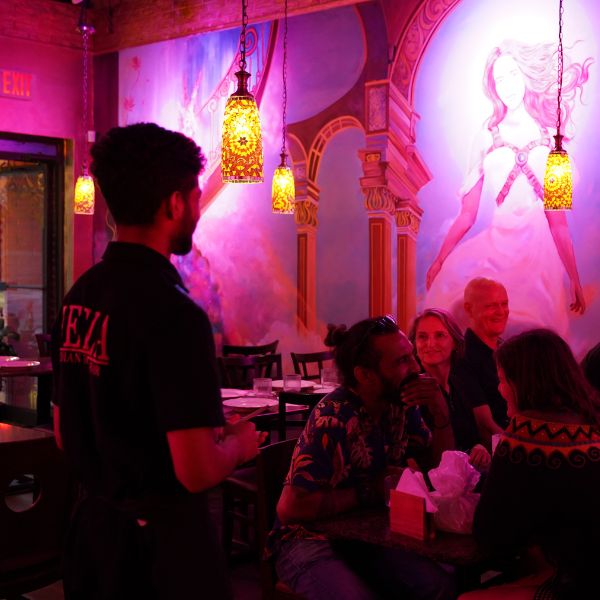 A man stands outside Leela Indian Food Bar, with diners enjoying their meals at tables in the vibrant atmosphere.