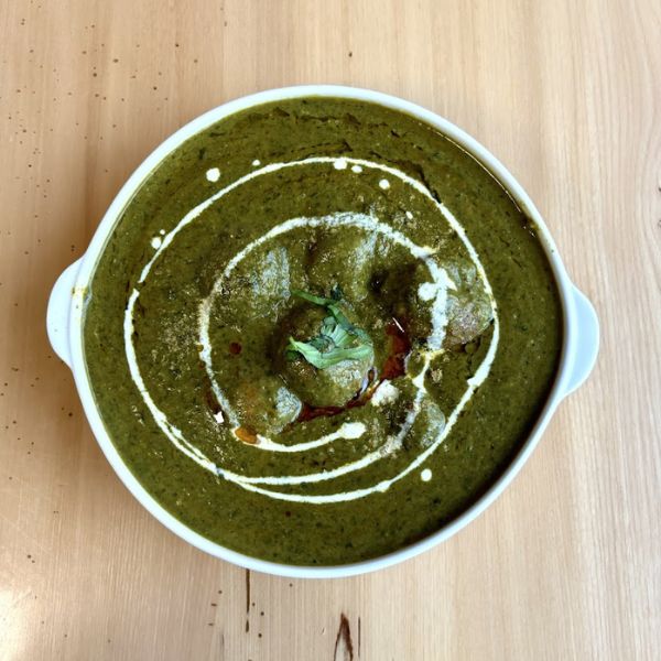 A bowl of vibrant green soup featuring a delicate white swirl, representing a flavorful blend of spinach and spices.